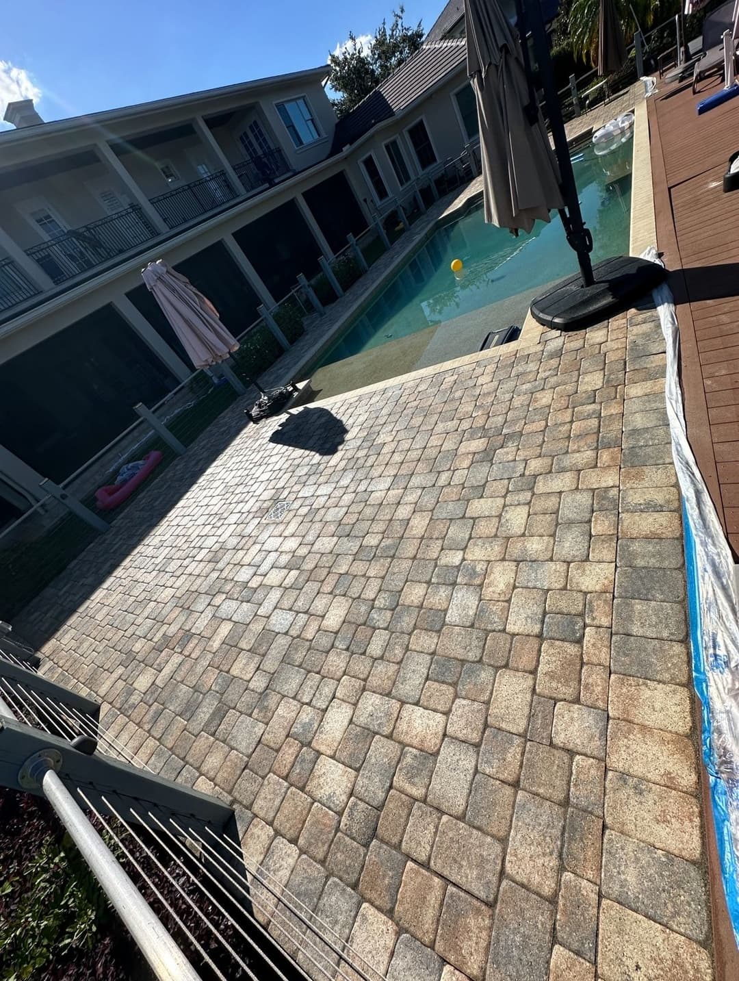 Backyard pool area with stone patio, lounge chairs, and vibrant landscaping under blue sky.