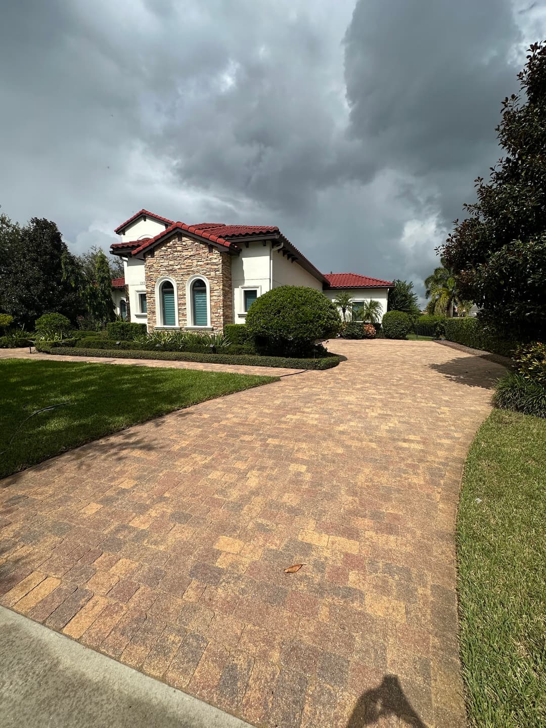 Elegant home with stone accents, red tile roof, and landscaped driveway under cloudy skies.