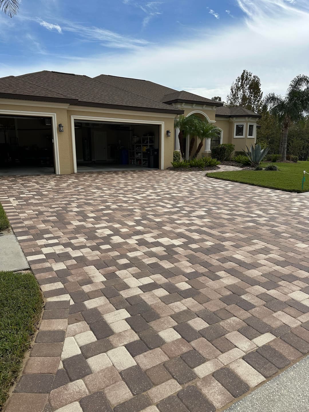 Paver driveway with a modern home and landscape under a clear blue sky.