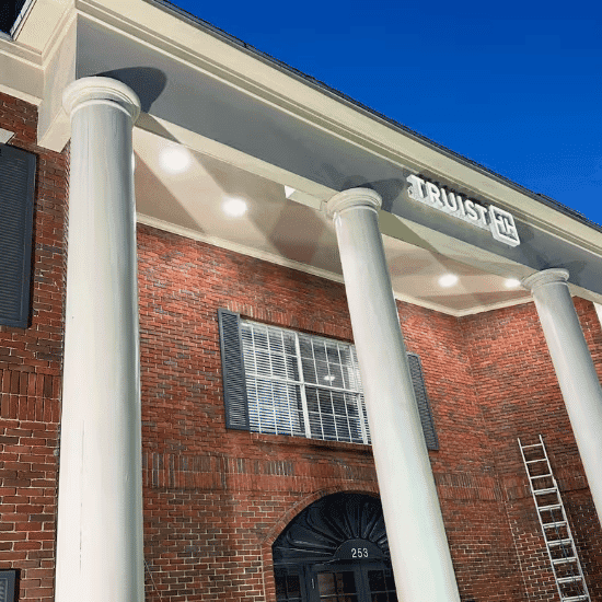 Historic brick building facade with columns and illuminated sign reading "TRUST."