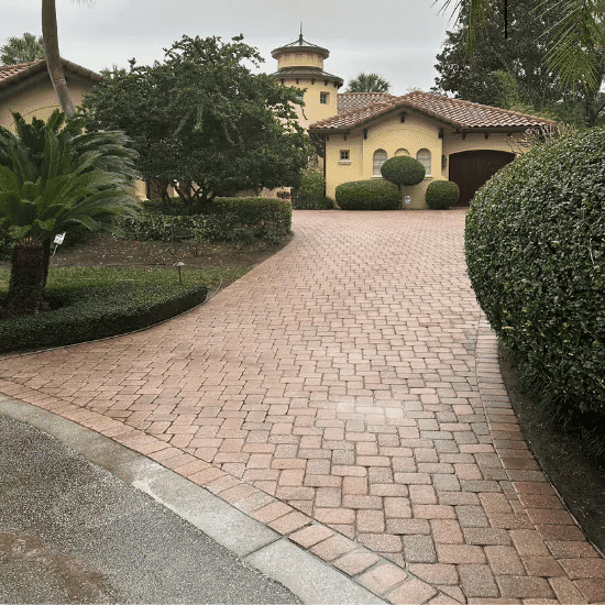Elegant paver driveway leading to a yellow stucco house surrounded by lush landscaping.