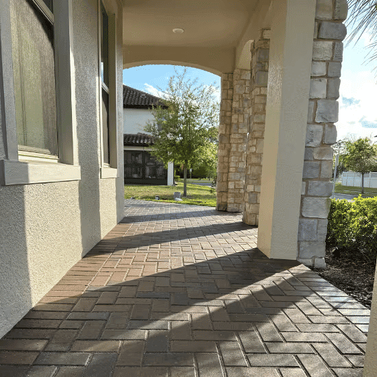 Paved walkway leading to an entrance with stone columns and lush landscaping.