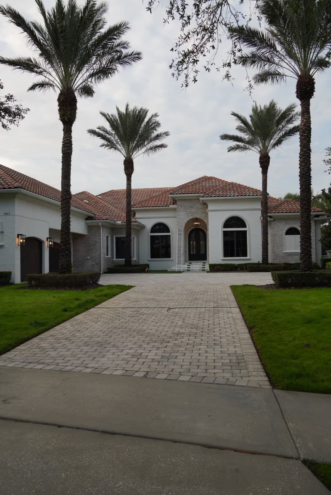 Luxury home with palm trees and paved driveway, featuring elegant architecture and a tiled roof.