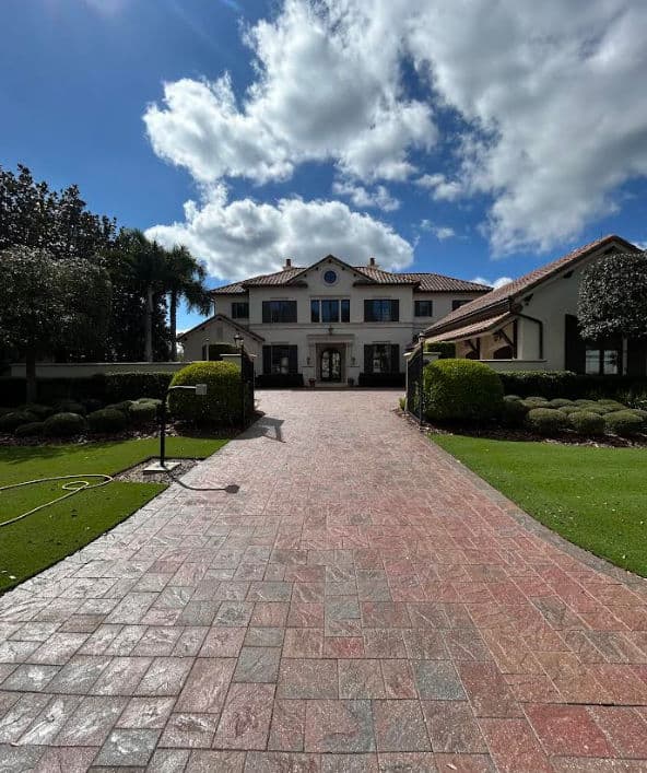 Spacious luxury home with a landscaped driveway under a blue sky and fluffy clouds.