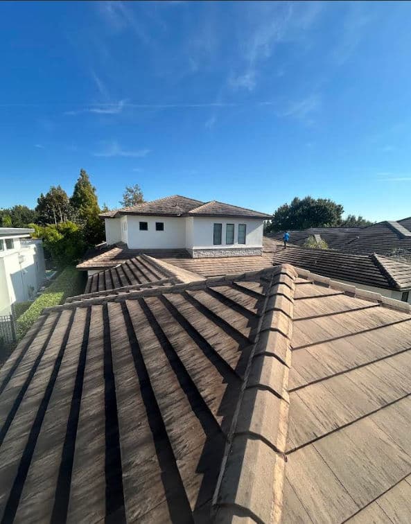 View of a residential roof showcasing brown tiles under a clear blue sky.