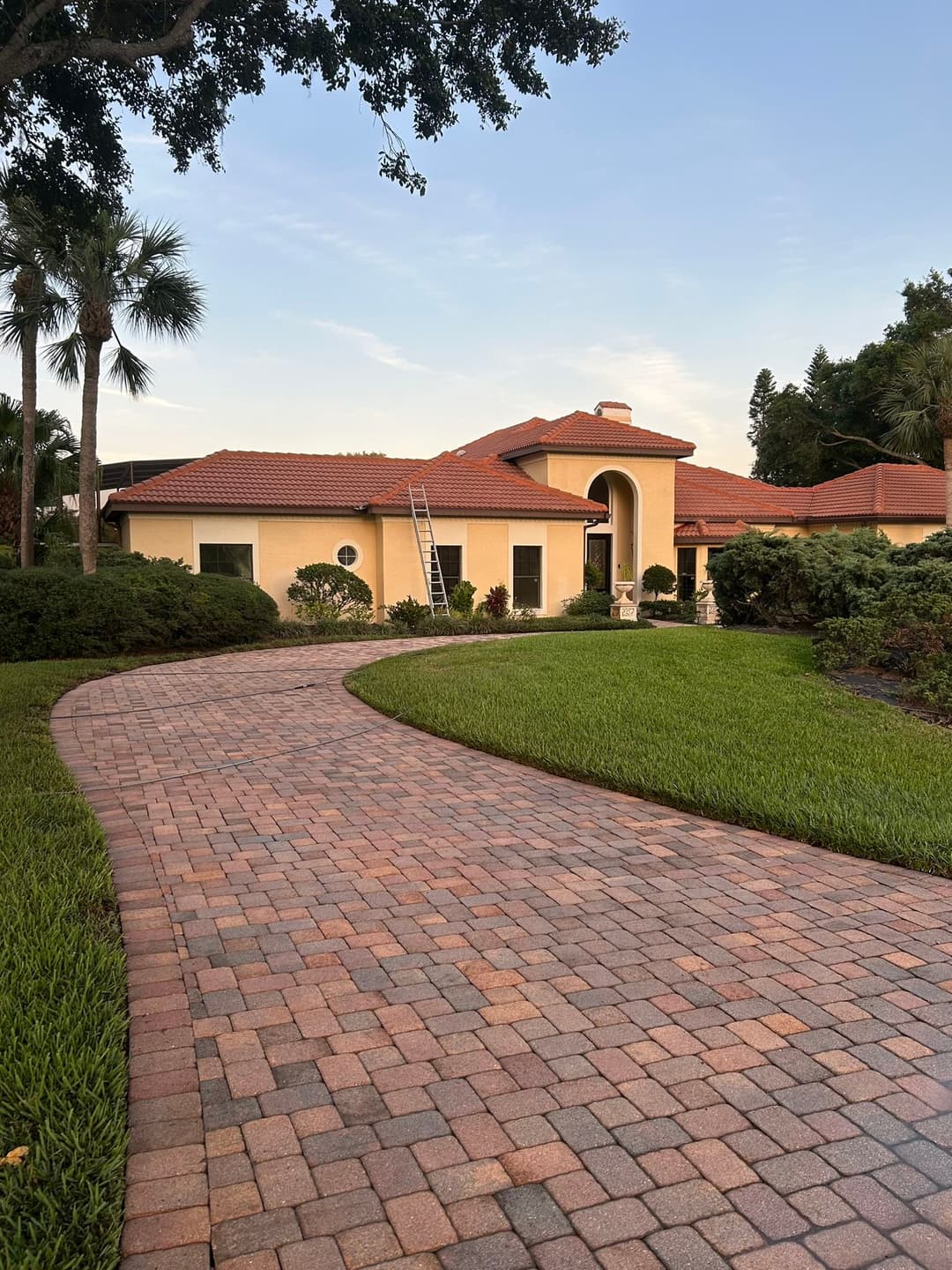 Beautiful modern home with red tile roof, landscaped yard, and brick pathway in sunlight.