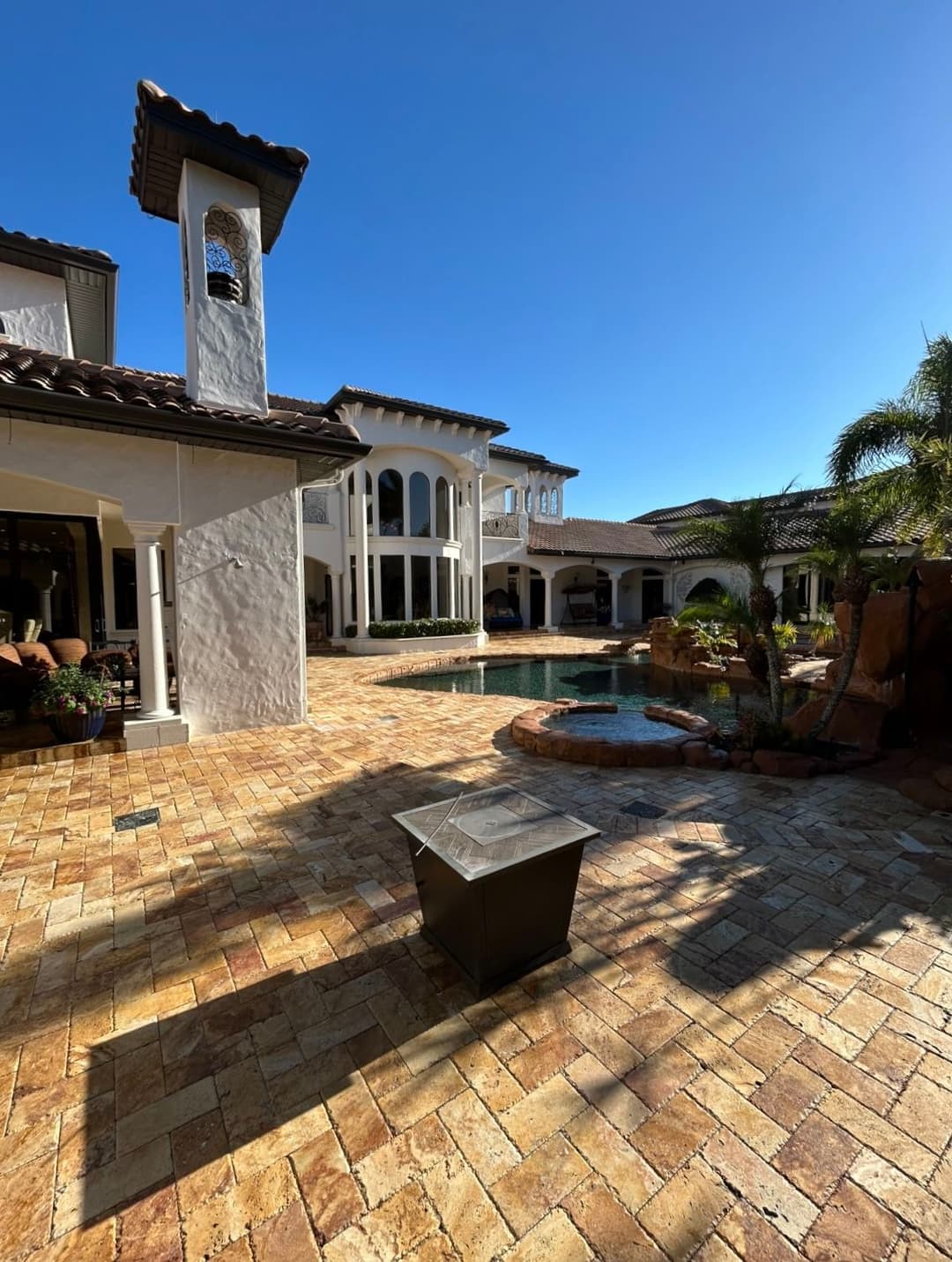 Luxury home exterior with pool, stone patio, and sunny blue sky. Elegant architecture.