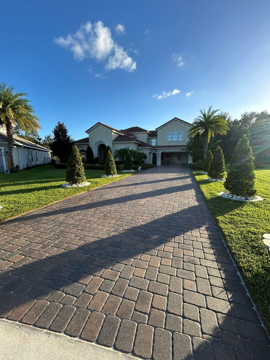 Luxury home with a paved driveway and palm trees under a clear sky.