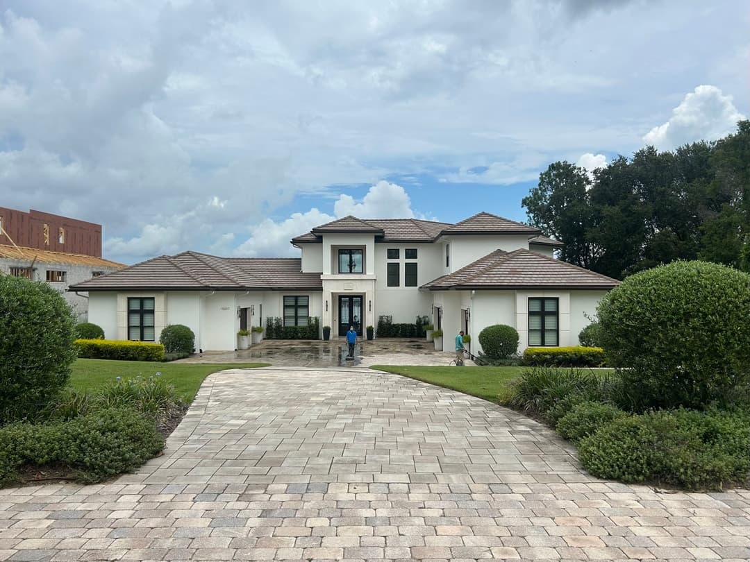Spacious modern home with landscaped front yard and stone driveway under a cloudy sky.