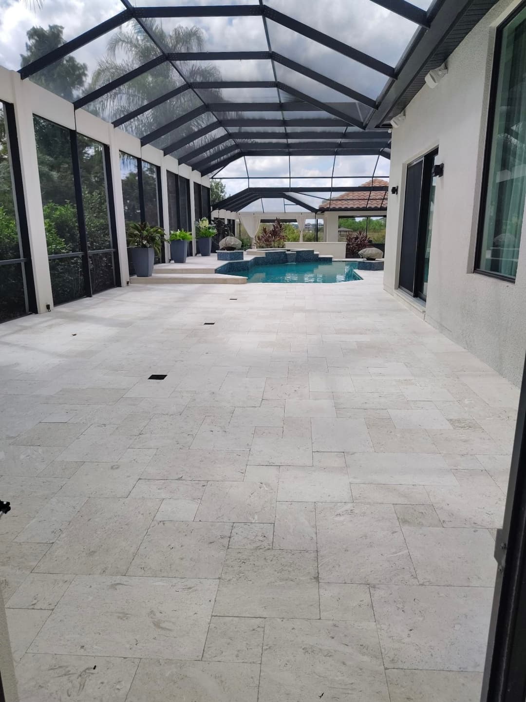 Modern screened patio with a pool, sunlight streaming, and elegant stone flooring.