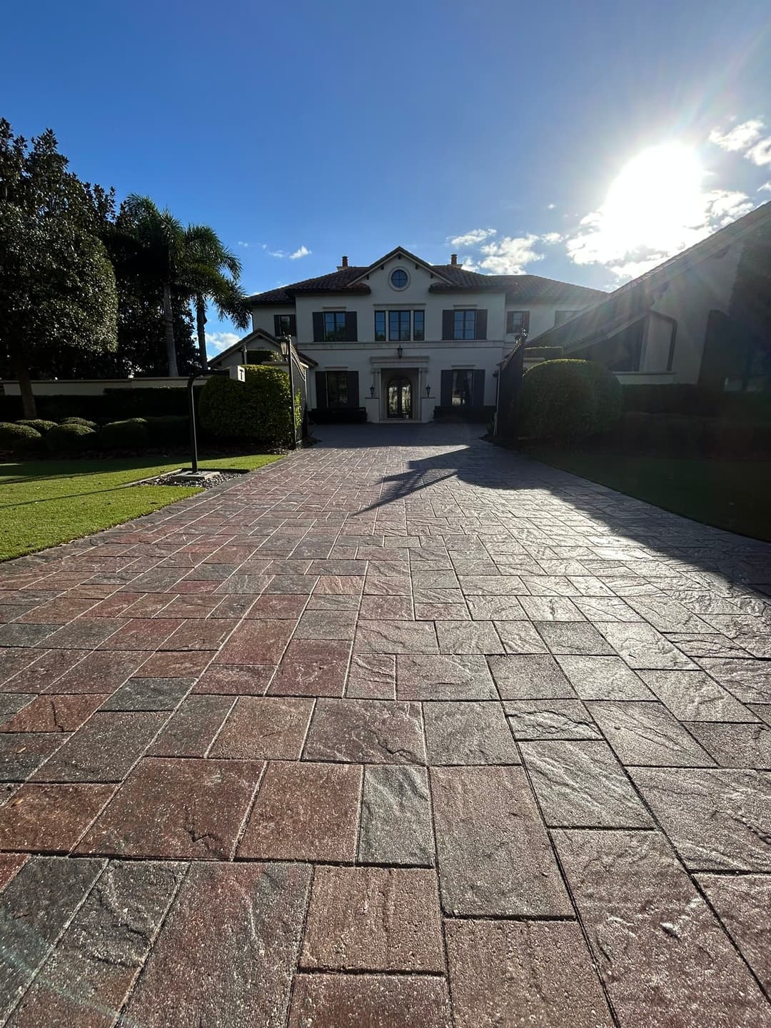Elegant house with a stone driveway, palm trees, and a bright sky in the background.